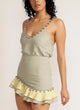 Close up of a woman stands in sage green skirt with pom pom trim and yellow and sage green ruffle detail with matching tank top