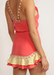 Close up of a back view of a woman in a watermelon pink skirt with pom-pom trim and yellow and pink ruffle detail and matching tank top