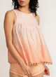 Close up of a woman wearing a dip-dyed sleeveless pink top with pom-pom trim and hand embroidered detail with pink shorts