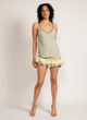Woman wears a sage green tank top with pom pom strap detail with matching skirt