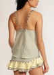 Back view of a woman wearing a sage green tank top with pom pom strap detail with matching skirt