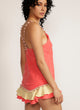 Side view of a woman wearing a pink camisole with pom pom strap detail and matching skirt