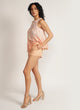 Side view of a woman wearing apricot shorts with pink piping detail and a pink top