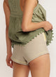 Close up of the back view of a woman wearing beige shorts with yellow piping detail and yellow lined pockets and a green top