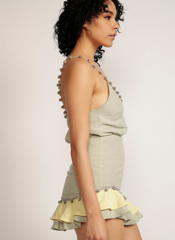 Close up of a woman's side profile wearing a sage green skirt with pom pom trim and yellow and sage green ruffle detail with matching tank top