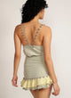 Back view of a woman standing in sage green skirt with pom pom trim and yellow and sage green ruffle detail with matching tank top