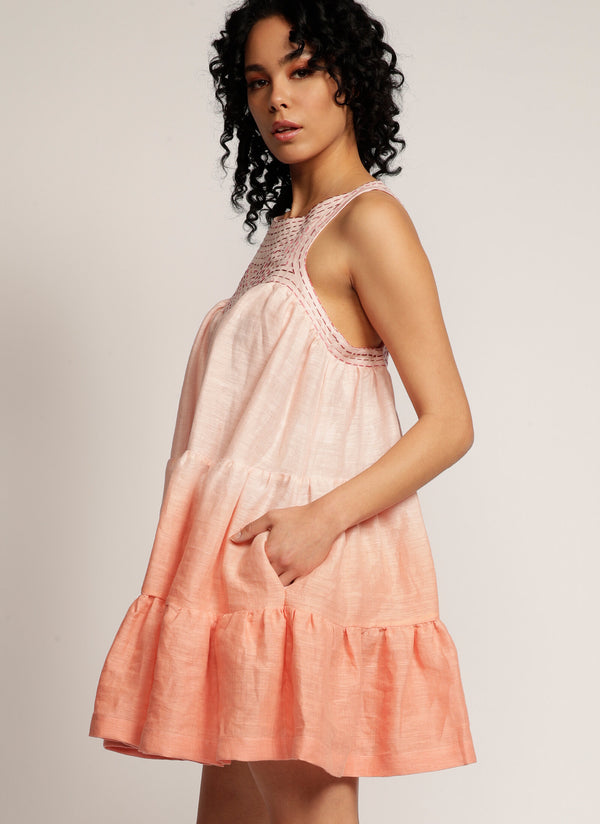 Side profile of a woman standing in a dip-dyed pink sleeveless dress with hand embroidered detail on the yoke