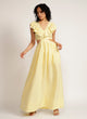 Woman wears a yellow maxi dress with cutout detail and ruffle neckline