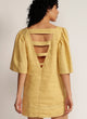 Back view of a woman wearing a yellow mini dress with V cutout detail