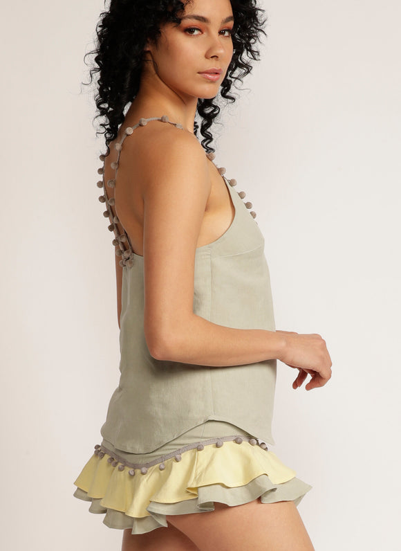 Side view of a woman wearing a sage green tank top with pom pom strap detail with matching skirt