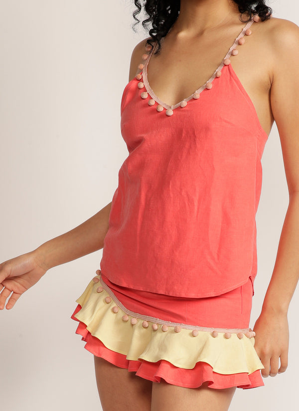 Close up of a woman wearing a pink camisole with pom pom strap detail and matching skirt